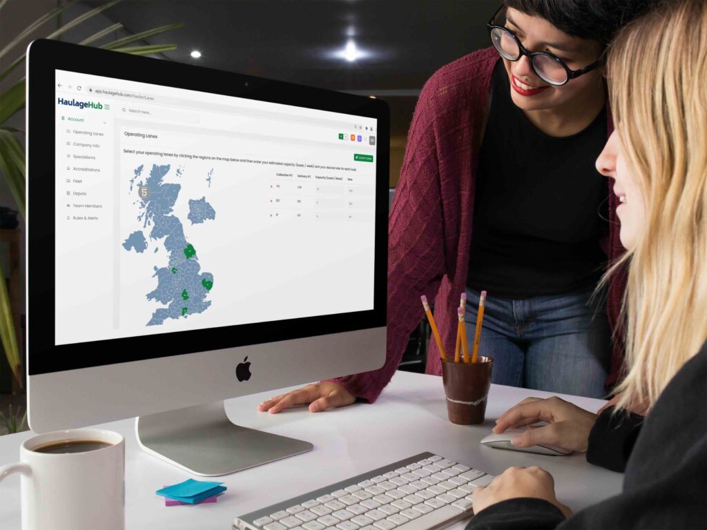 Two people using the HaulageHub platform on a desktop computer, viewing a map of operating lanes and transport data